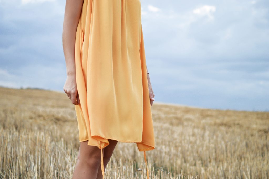 A woman wears a light, feminine orange dress in a golden field.