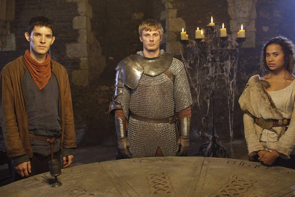 Merlin, Arthur, and Gwen all stand around the round table.