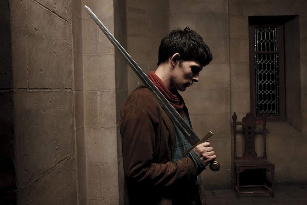 Merlin holding a sword, his face bent down and hidden in shadow