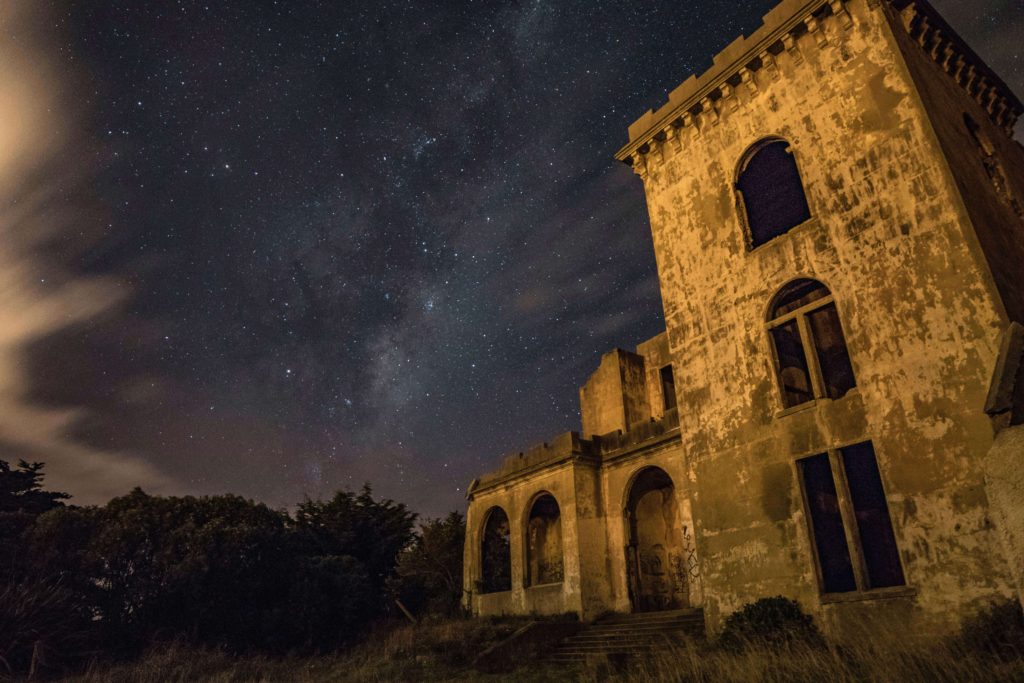 An old, yellow church building with gaping, dark windows, framed by a starry night sky.