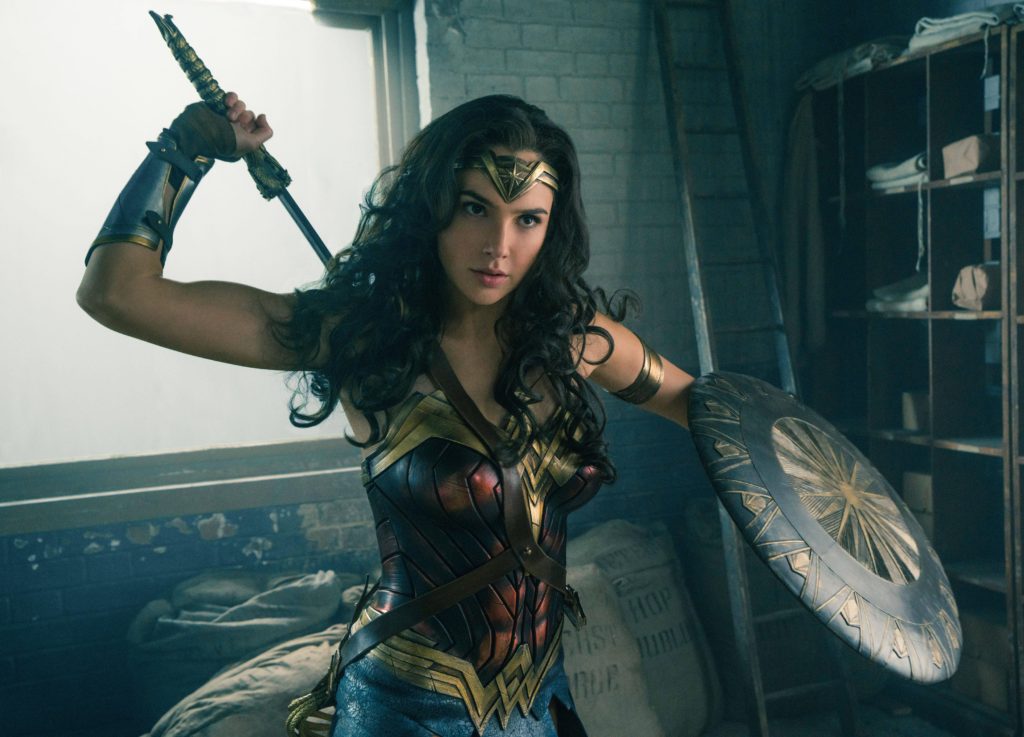 Gal Gadot as Wonder Woman, pulling the sword from her back, mid-action. Her long, silky, wavy hair makes her look very feminine, but in this frame she's about 2 seconds away from seriously kicking ass. And these two facts are not contradictory.